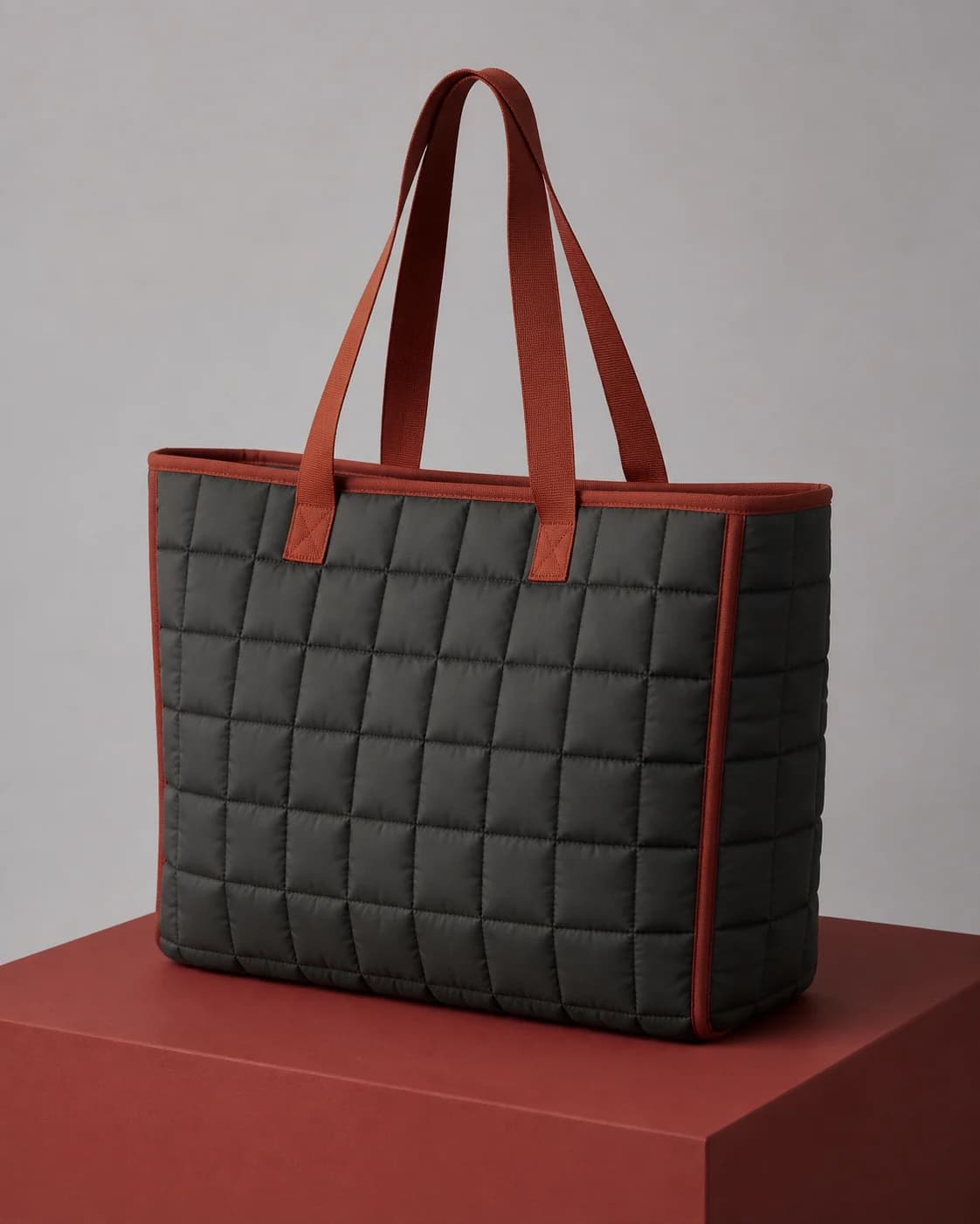 AI concept of an unbranded graphite quilted tote with oxide-red binding.