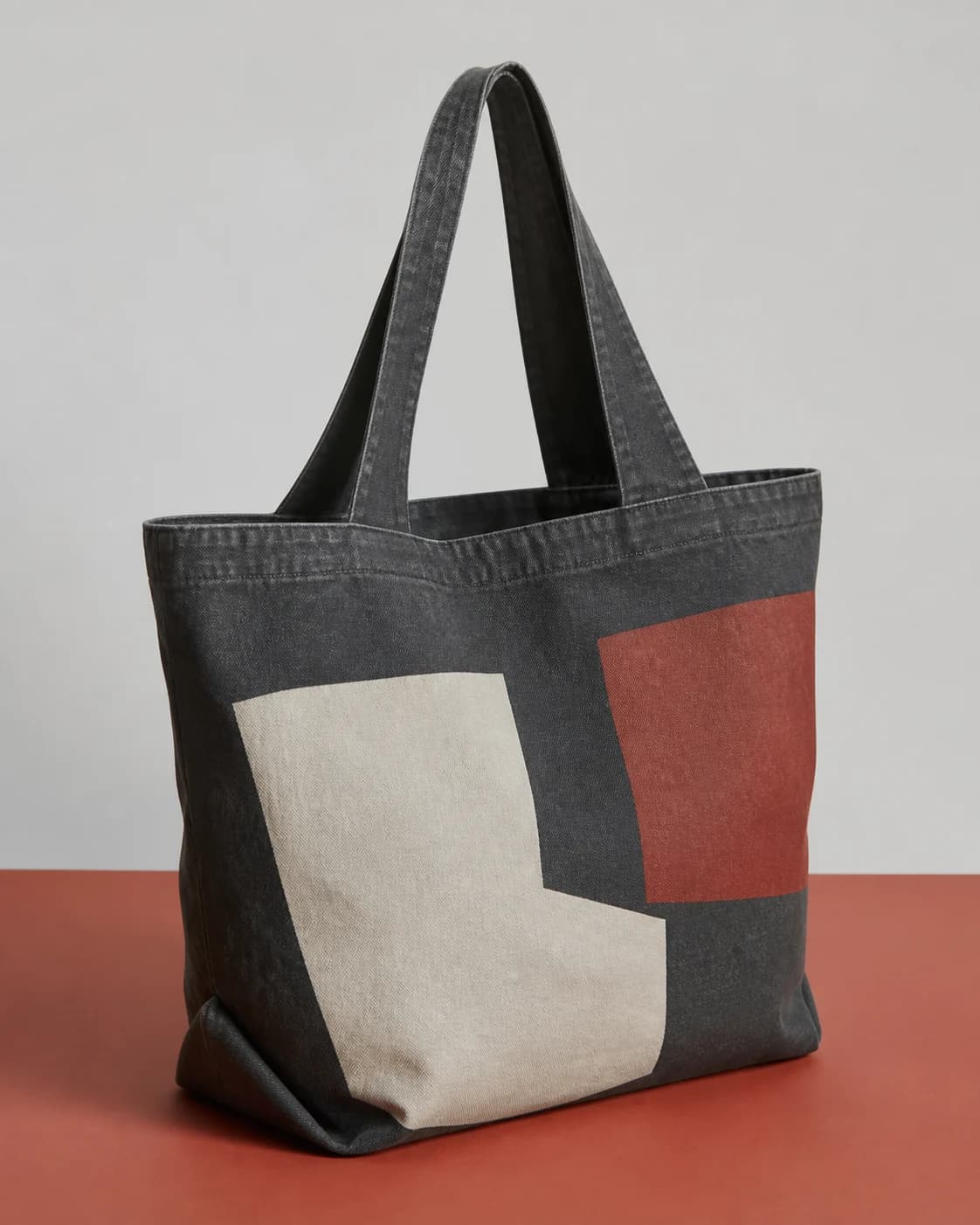 AI concept of an unbranded washed charcoal canvas shopper with abstract blocks.
